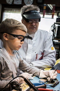 Worker looking at boy repairing equipment in workshop