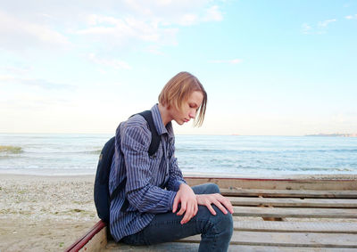 Man sitting at beach against sky