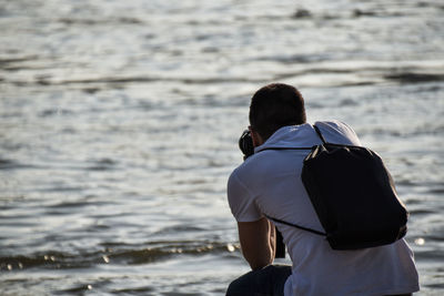 Rear view of man photographing while crouching at beach