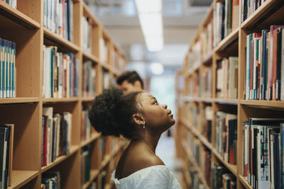 Side view of student searching books on bookshelf in library at university