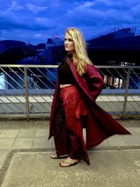 Young woman standing by railing against sky