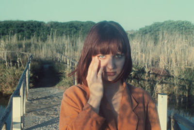 Portrait of young woman crying while standing on bridge over river