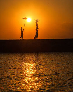 Silhouette people standing by sea against sky during sunset