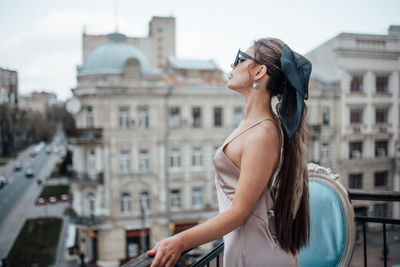 Side view of young woman standing against buildings in city