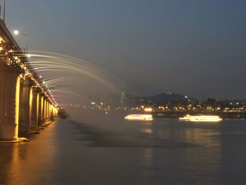 Illuminated city by river against sky at night