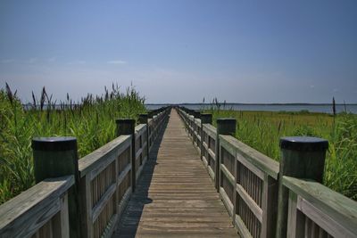 Boardwalk with railing leading towards river against sky