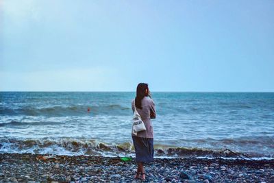 Rear view of man standing at beach against sky