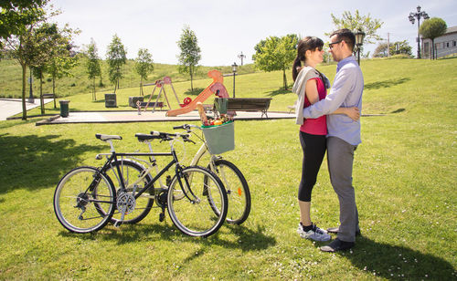 Full length of happy couple embracing by bicycle in park during summer