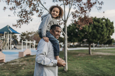 Cute boy sitting on happy father's shoulders at park playground