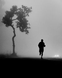 Silhouette man walking on field against sky at dusk