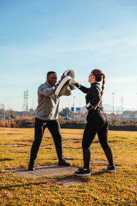 Full length of woman and man exercising on field against sky