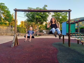 Full length of mother and son swinging in playground