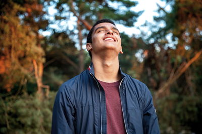 Smiling young man standing against trees