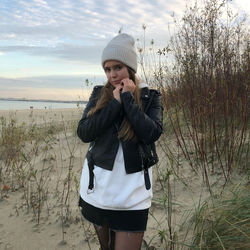 Portrait of young woman standing on beach against sky