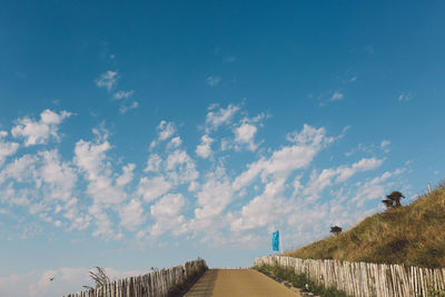 Empty walkway at beach against blue sky