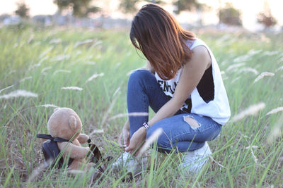 Young woman tying shoelace by teddy bear on grassy field