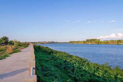 Footpath by sea against blue sky