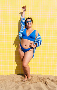 Portrait of young woman wearing bikini standing against wall