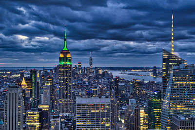 Illuminated buildings in city against cloudy sky