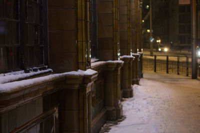 Snow covered footpath by building in city at night