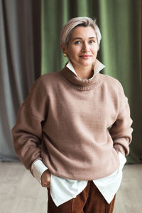 Fashion woman in brown oversize sweater and trousers standing in modern work place or office