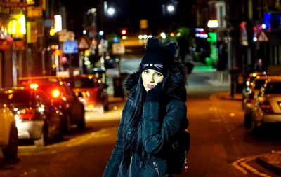 Portrait of young woman wearing warm clothing while standing on street at night