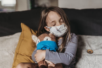 Preschool age girl with mask on cuddling stuffed animal with mask