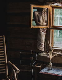 Shirtless woman reflecting on mirror by window at home