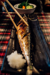Chopsticks holding grilled fish on table