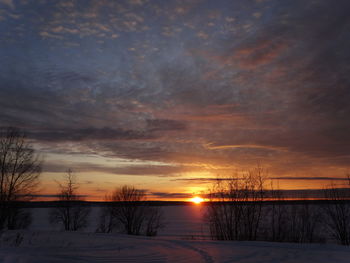 Snow covered landscape against sky during sunset