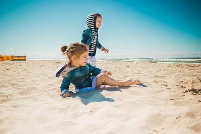 Siblings playing with sand at beach against sky