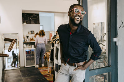 Smiling owner with hands in pockets standing at doorway of clothing store