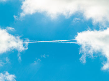 Low angle view of vapor trail and clouds in blue sky