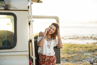 Happy woman talking on mobile phone by off-road vehicle at beach