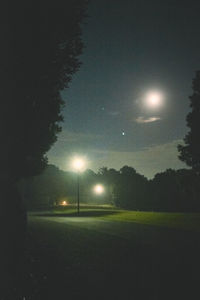 Illuminated street light on field against sky at night