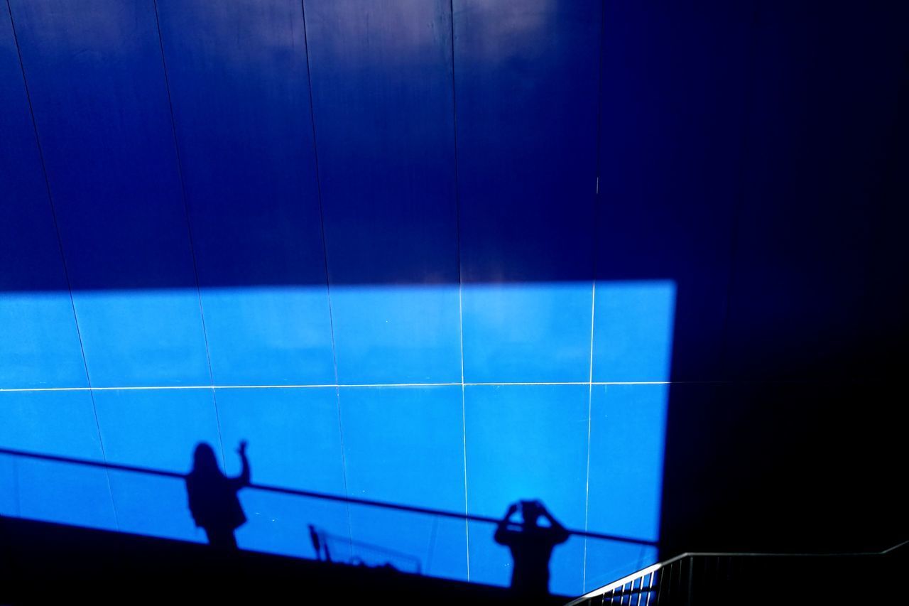 SILHOUETTE OF MAN PLAYING IN ILLUMINATED BLUE WALL