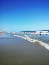 People enjoying at beach against clear blue sky