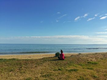 Woman sitting on beach against blue sky