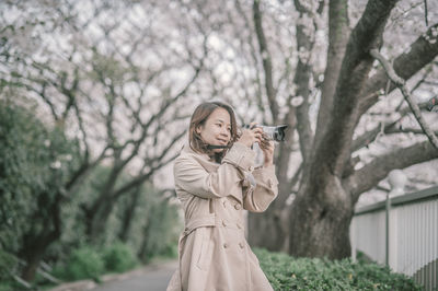 Smiling woman photographing with digital camera while standing in park