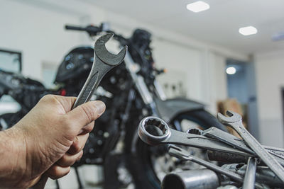 Cropped hand of mechanic holding wrench standing in garage