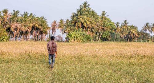 Rear view of woman walking on field against sky