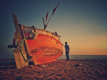 Full length of man standing by boat at beach during sunset