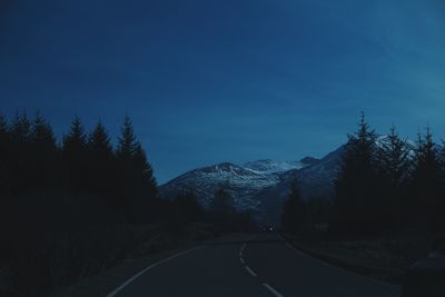 Road by trees against blue sky at dusk