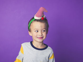 Smiling boy wearing party hat against purple background