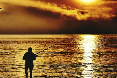 Silhouette man fishing in sea against sunset sky