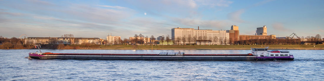 Nautical vessel on river by buildings in city against sky