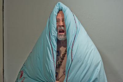 Portrait of young man lying on bed against wall