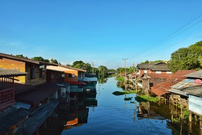 Buildings by river against clear blue sky