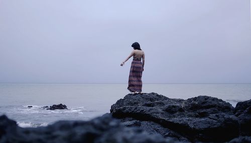 Rear view of woman standing on rock by sea