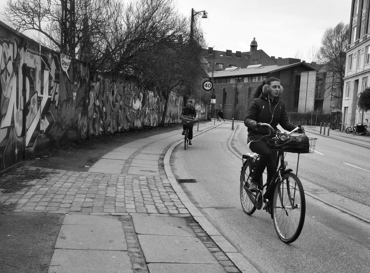 bicycle, transportation, land vehicle, mode of transport, building exterior, street, architecture, built structure, riding, city, men, road, lifestyles, full length, city life, walking, stationary, cycling, the way forward